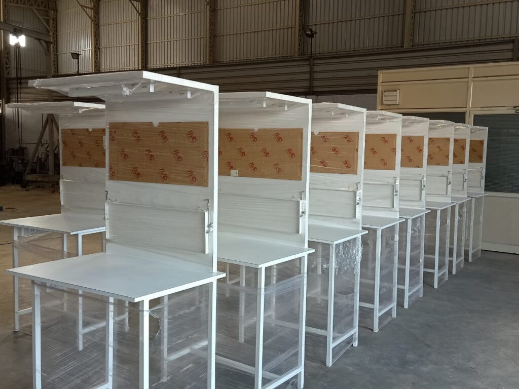 Features of MS Work Tables with Wooden Tops: Mild Steel Frame: The structure of these tables is made from Mild Steel (MS), a durable and cost-effective material. The steel frame provides the necessary strength and stability for various industrial or workshop settings. Wooden Top: The tabletop is made of wood (often plywood, MDF (Medium Density Fiberboard), or hardwood), offering a sturdy and smooth surface for work. Wood adds a functional and aesthetic element to the table, making it suitable for a range of activities, from office tasks to light industrial work. Durability: The combination of steel and wood offers a balance of strength and resilience. The steel frame can withstand heavy loads, while the wooden top provides a smooth, flat surface for various activities. Adjustability: Some models may come with adjustable heights, allowing for ergonomic settings. This is beneficial for ensuring comfort during use. Design & Functionality: These tables are typically designed for workshops, laboratories, office spaces, or even home offices, where you need a solid surface for tasks like assembly, drawing, or computer work. They can also feature drawers, shelving, or cabinets for storage. Finish Options: The steel frame may be finished with a powder-coated layer for corrosion resistance, while the wood can have various finishes like laminate, polished, or matte for a more refined look. Common Uses: Workshops: Ideal for assembly, crafting, or other detailed manual work. Offices: Can be used as desks, especially in industrial-style office designs. Laboratories: Perfect for lab tasks due to the strong surface and stable base. Storage Areas: Some versions may incorporate shelves or drawers for easy storage of tools and equipment. Buying Considerations: Load Capacity: Ensure the table can handle the weight of the tools or materials you will use. Size: Choose dimensions that fit your workspace, ensuring enough legroom and space for work. MS Work Tables With Wooden Top (2)